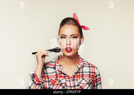 Überrascht Pin-up-Girl in Plaid Shirt holding Make-up Pinsel. retro style Frau Anwendung blusher. Kopieren Sie Platz für Text Stockfoto