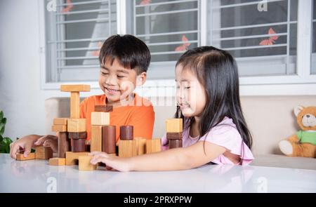 Glückliche kleine Kinder spielen Holzblock Stapeln Brettspiel zu Hause, Kinder Junge und Mädchen spielen mit Konstruktor Holzblock, Kindheitsaktivitäten lernen Stockfoto