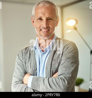 Erfolg in Schritt. Porträt eines lächelnden, reifen Geschäftsmanns, der mit gekreuzten Armen in einem Büro steht Stockfoto