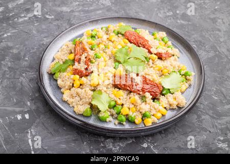 Quinoa-Haferbrei mit grüner Erbse, Mais und getrockneten Tomaten auf Keramikplatte auf grauem Betongrund. Seitenansicht, Kopierbereich. Stockfoto