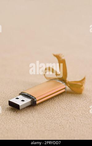 Orange usb Flash Memory Card mit blauer Schleife liegt auf einer Decke aus weichem und haarige Licht orange Fleece Stoff. Klassische weibliche Geschenk Design für ein Memory c Stockfoto