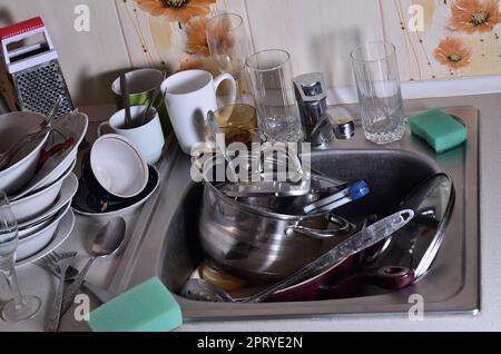 Ein riesiger Haufen ungewaschenen Geschirr in der Spüle und die Arbeitsplatte. Eine Menge Geschirr und Küchengeräte vor dem Waschen. Das Konzept der Zähler Stockfoto