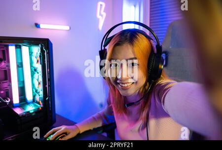 Live-Stream. Asiatische Frau, die zu Hause Gaming-Kopfhörer trägt, Happy Gamer aufnimmt und ihre Online-Fans während des Live-Streamings vor pla begrüßt Stockfoto