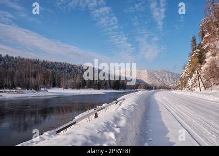 Altai Winterstraße und Fluss Biya in der Wintersaison. Die Flussufer sind mit Eis und Schnee bedeckt. Altai, Sibirien, Russland Stockfoto