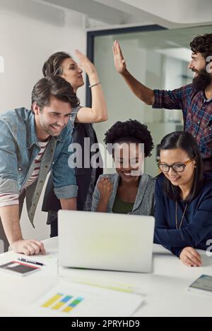 Wir wurden schließlich für beste Zusammenarbeit ausgezeichnet. Eine Gruppe von Designern, die sich etwas auf einem Laptop ansehen Stockfoto