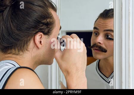 Nicht-binäre junge Latino-Person in ihrem Zimmer, die sich im Spiegel spiegelt und ihre Wimpern, ihr Schönheitskonzept, ihren Kopierraum definiert. Stockfoto