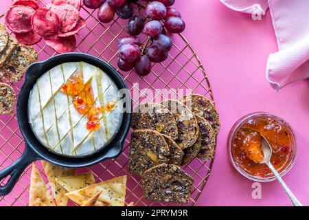 Gebackener Brie-Käse in einer gusseisernen Pfanne, umgeben von verschiedenen Pendeln. Stockfoto