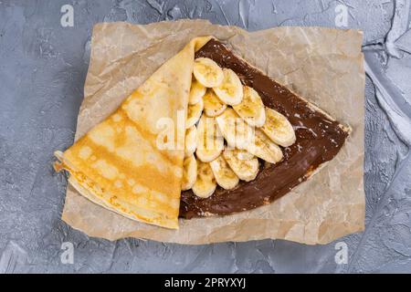 Crepes gefüllt mit Schokolade und Banane auf weiße Platte. Dünne Pfannkuchen, Blini. Süße Nachspeise. Stockfoto