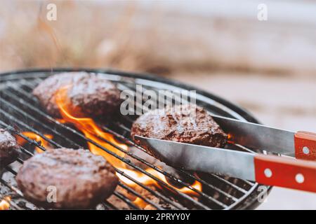 Nahaufnahme Foto eines Grills auf dem Hinterhof. Party Im Freien. Leckeres, saftiges Fleisch für Burger, gekocht auf Feuer. Traditionelle Küche der Vereinigten Staaten von Amerika. Stockfoto