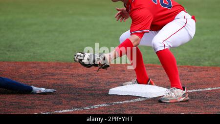 Dritter Baseman, bereit, den Arm eines gleitenden Läufers während eines Highschool-Baseballspiels auszustechen. Stockfoto