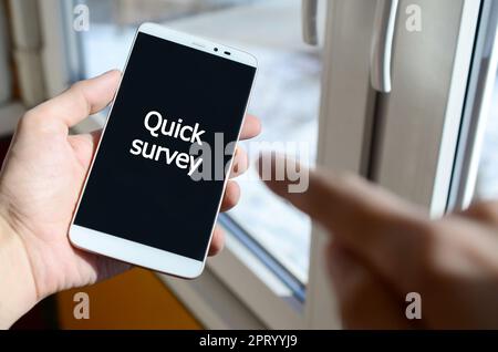 Eine Person sieht eine weiße Inschrift auf einem schwarzen Smartphone-Display, das in ihrer Hand hält. Kurze Umfrage Stockfoto