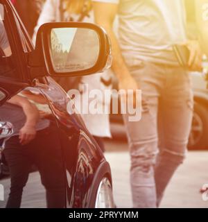 Diagonalansicht eines schwarz glänzenden Autos mit weißen Rädern, das auf einem Quadrat grauer Fliesen steht Stockfoto