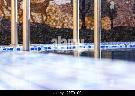 Eine Metall Swimming Pool Safe Leiter (Skimmer) am Eingang zum Haus auf der Poolseite mit dem blauen sauberen Wasser. Stockfoto