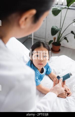 Verschwommener Kinderarzt zeigt Inhalator zu überraschenden asiatischen Kind auf der Krankenstation, Stock Image Stockfoto