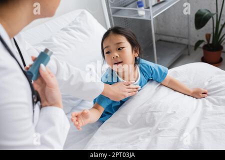 Neugieriges asiatisches Mädchen mit ausgestreckter Hand erreicht Arzt mit Inhalator im Krankenhaus, Stock Image Stockfoto