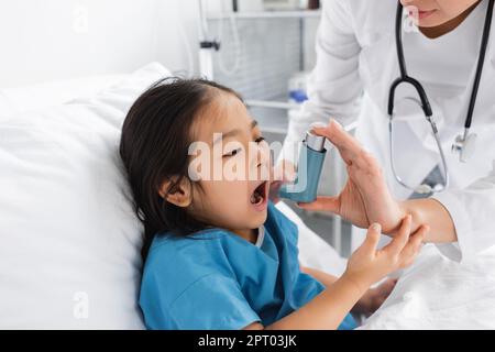 asiatisches Mädchen, das den Mund in der Nähe eines Arztes öffnet und Inhalator in der Kinderklinik benutzt, Stock-Bild Stockfoto