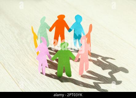 Viele verschiedene Papiermenschen stehen im Kreis auf einem weißen Holztisch. Diversitäts- und Integrationskonzept Stockfoto