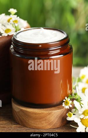 Ein Glas Handcreme und Kamille auf einem Holztisch, Nahaufnahme Stockfoto