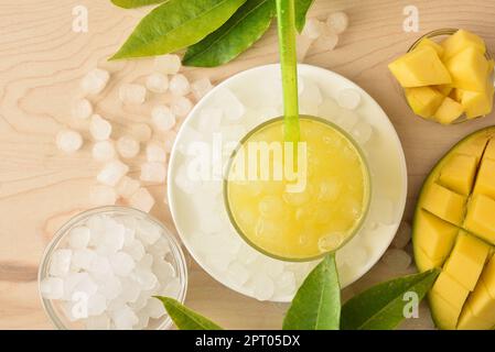 Detail aus Glas mit kaltem Mangogetränk auf dem Teller mit Eis und Obst. Draufsicht. Horizontale Zusammensetzung. Stockfoto