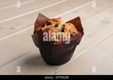 Frischer Muffin mit Schokoladenstückchen in Papierverpackung auf einem Holztisch Stockfoto