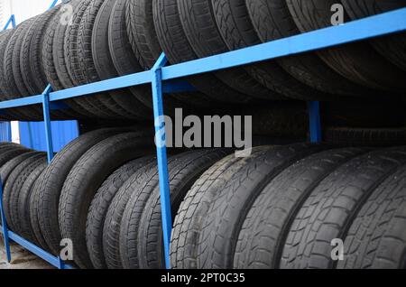 Rack mit verschiedenen Autoreifen im Automobilgeschäft. Viele schwarze Reifen. Hintergrund des Reifenstapels. Selektiver Fokus Stockfoto