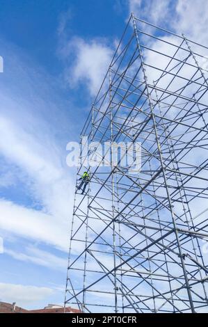 Unidentifizierter Arbeiter in der Höhe, der einen Gerüstturm demontiert. Blauer wolkiger Himmel im Hintergrund Stockfoto