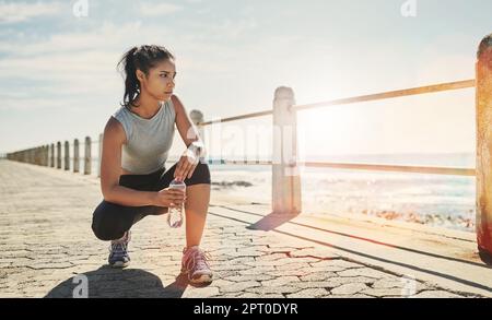 Fühlen Sie sich wieder voller Energie. Eine junge sportliche Frau, die sich draußen hockt Stockfoto