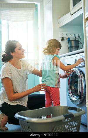 Sie ist eine neugierige kleine. Ein kleines Mädchen, das ihrer Mutter beim Waschen hilft Stockfoto