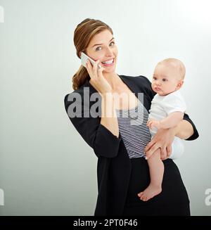 Es lohnt sich, hart für mein Baby zu arbeiten. Eine erfolgreiche junge Geschäftsfrau, die ihren niedlichen kleinen Jungen trägt, während sie telefoniert Stockfoto