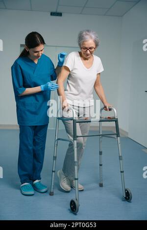 Junge Krankenschwester begleitet eine ältere Frau in der Klinik Stockfoto