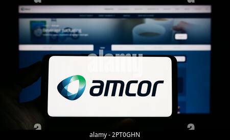 Person, die ein Mobiltelefon mit dem Logo des Verpackungsunternehmens Amcor plc auf dem Bildschirm vor der geschäftlichen Webseite hält. Konzentrieren Sie sich auf das Display des Telefons. Stockfoto