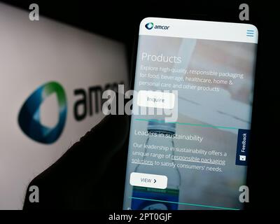 Person, die ein Mobiltelefon mit dem Logo des Verpackungsunternehmens Amcor plc auf dem Bildschirm vor der geschäftlichen Webseite hält. Konzentrieren Sie sich auf das Display des Telefons. Stockfoto