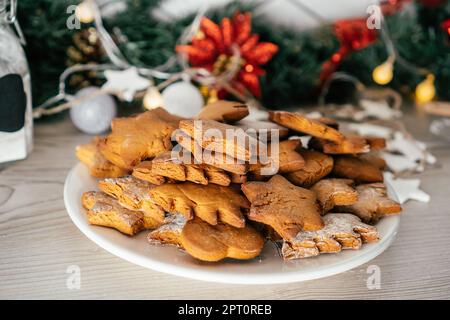 Teilweise verschwommener Teller mit Lebkuchenkuchen in Form von weihnachtsbäumen, Sternen und Herzen stehen auf der Küchenarbeitsplatte vor christm-Hintergrund Stockfoto