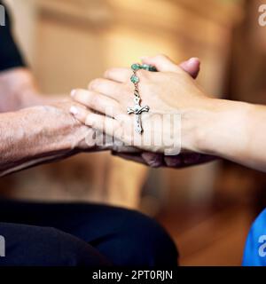 Vereint durch Glauben. Eine Person, die mitfühlend einen Rosenkranz hält, und eine ältere Frau, die Hände hält Stockfoto