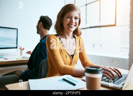 Ich schaffe meinen eigenen Erfolg. Abgeschnittenes Porträt einer attraktiven jungen Geschäftsfrau, die in einem modernen Büro an ihrem Laptop arbeitet. Stockfoto