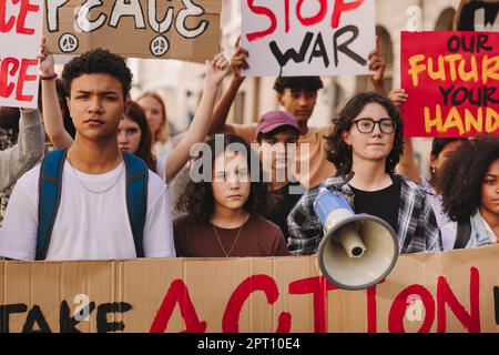 Jugendaktivisten, die während einer Anti-Kriegs-Kundgebung Banner und Plakate hochhielten. Gruppe multikultureller junger Menschen, die für den Weltfrieden marschieren. Teenager-Dämonen Stockfoto