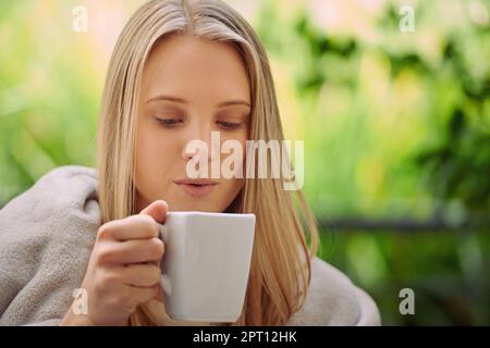 Die einzige Möglichkeit, mich aufzuwecken. Eine junge Frau, die draußen eine Tasse Kaffee trinkt Stockfoto