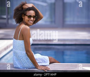 Ich würde nirgendwo anders sein wollen als hier. Voller Schuss einer attraktiven ethnischen Frau, die am Pool posiert Stockfoto