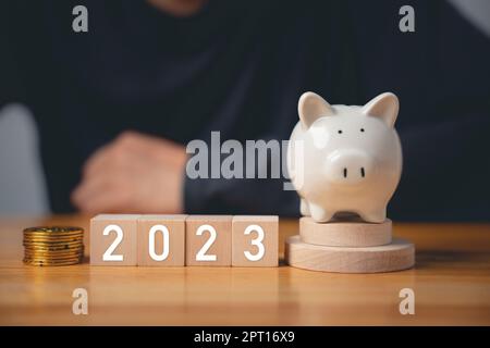 Frohes Neues Jahr 2023. Geschäftsmann mit Holzwürfeln, Baujahr 2023, und Sparschwein, um das Geschäftsziel zu setzen, Start Finance Success Bu Stockfoto