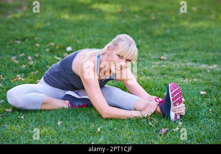 Die Welt ist aus diesem Blickwinkel wunderschön. Eine junge Frau, die sich auf einem grasbedeckten Feld streckt Stockfoto