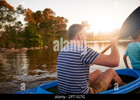 Paddeln in den Sonnenuntergang. Ein Vater und Sohn rudern zusammen auf einem See Stockfoto