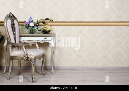 Ein Fragment eines retro Interieur mit einem Sessel und einen Schreibtisch, auf dem ein Telefon und eine Vase mit Blumen befindet. Stockfoto