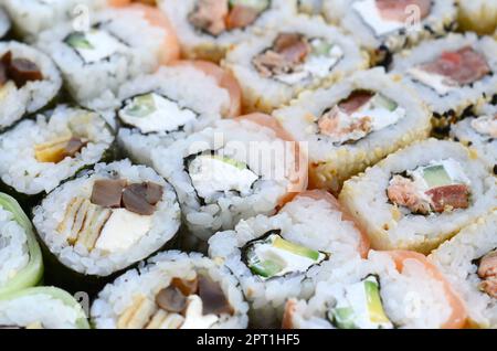 Nahaufnahme von vielen Sushi-Brötchen mit verschiedenen Füllungen. Makroaufnahme von gekochtem klassischem japanischem Essen. Hintergrundbild Stockfoto