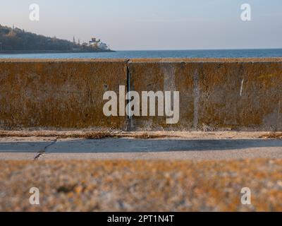 Blick von der Promenade mit alten Betonblöcken über das ruhige blaue Wasser des Kiew-Meeres und Hügels mit einem Wasserkraftwerk am Horizont Stockfoto