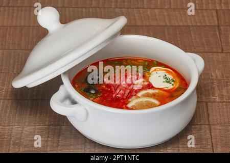 Soljanka - russische traditionelle Fleischsuppe. Russische Suppe Mönchsbart in Runde Platte auf hölzernen Hintergrund. Stockfoto