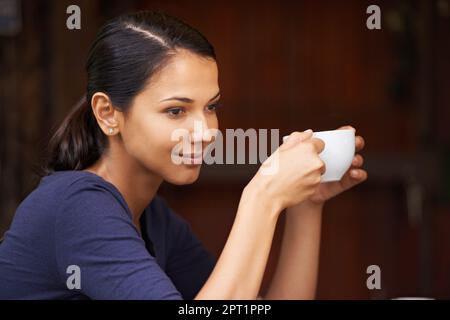 Die Wärme sinkt ein. Eine junge Frau, die draußen eine Tasse Kaffee trinkt Stockfoto