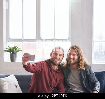 Zwillingsbrüder machen Fotos mit dem Smartphone, wenn sie zu Hause auf dem Sofa sitzen. Stockfoto