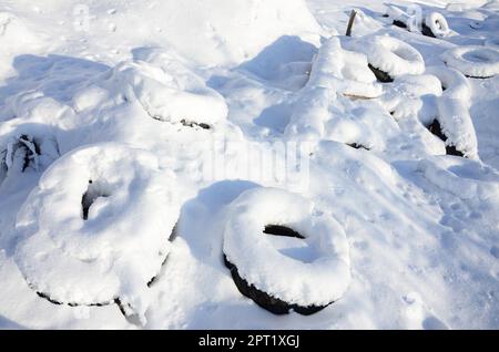 Gebrauchte und entsorgte Autoreifen liegen am Straßenrand und sind mit einer dicken Schneeschicht bedeckt Stockfoto