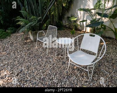 Weißer Metallstuhl und Tisch für Kaffeezeit im tropischen Garten, entspannende Zeit am Morgen, Vorderansicht mit Kopierbereich. Stockfoto