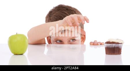 Hmmm... was zu tun ist. Ein bösartiger Junge, der an einen Tisch guckt, auf dem ein Cupcake und ein Apfel stehen Stockfoto